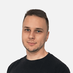 Portrait of a person with short hair, a trimmed beard, and wearing a black shirt, set against a plain, light-colored background.
