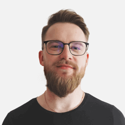 A man with a beard and glasses is smiling slightly. He is wearing a black shirt and is set against a plain white background.