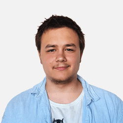 A person smiling, wearing a light blue shirt over a white T-shirt, against a plain white background.