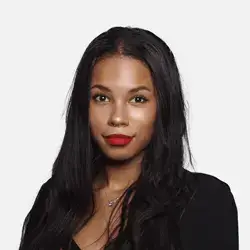 Portrait of a person with long, dark hair and red lipstick, wearing a black top. The background is plain and light-colored.