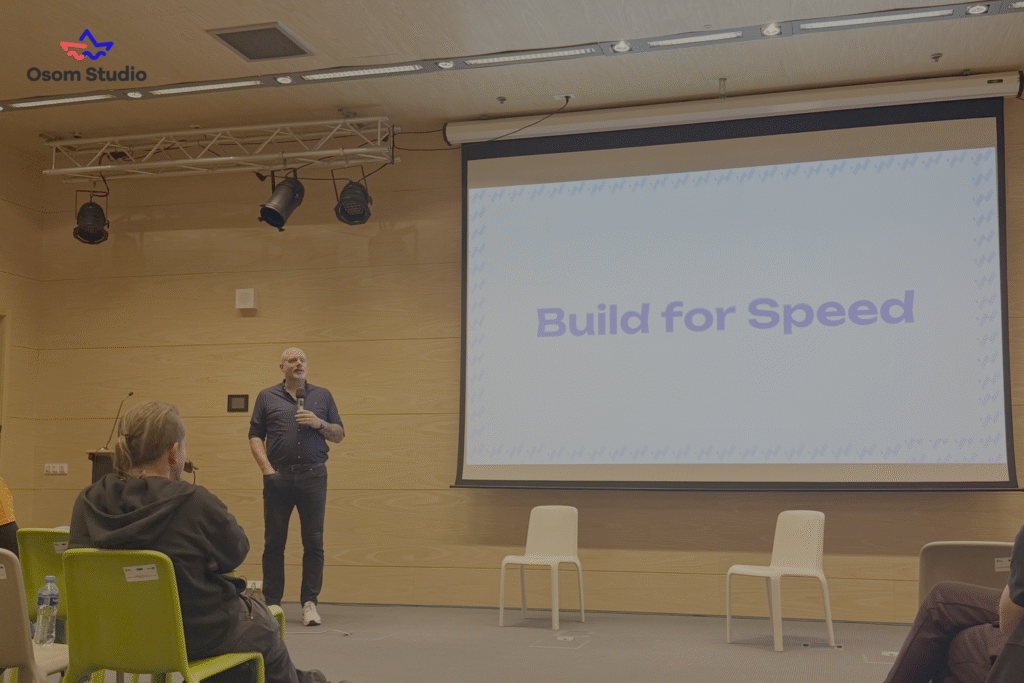 A man stands on stage at WordCamp, speaking in front of a screen displaying the text “Build for Speed” to an audience seated in a modern room. The Osom Studio logo is visible in the top left corner.