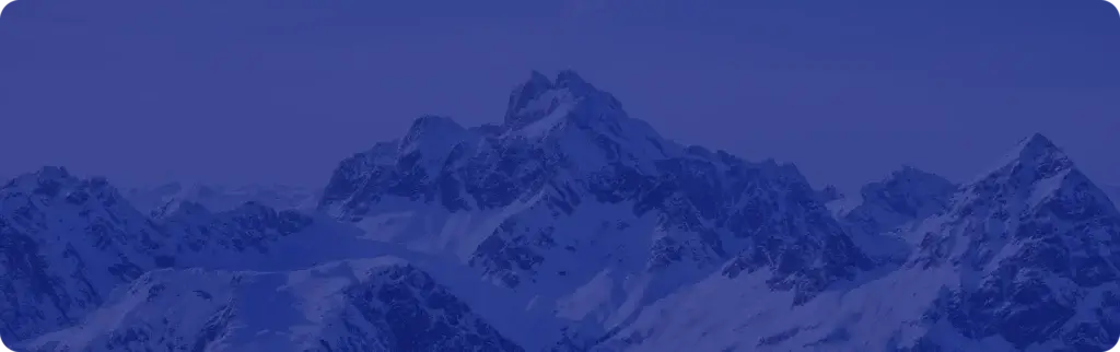 Snow-covered mountain peaks under a clear sky, bathed in bluish light.