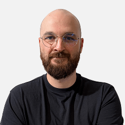 A bearded man with glasses and a bald head, wearing a black t-shirt, stands against a plain white background with arms crossed, ready to build your next WordPress website at Osom Studio.